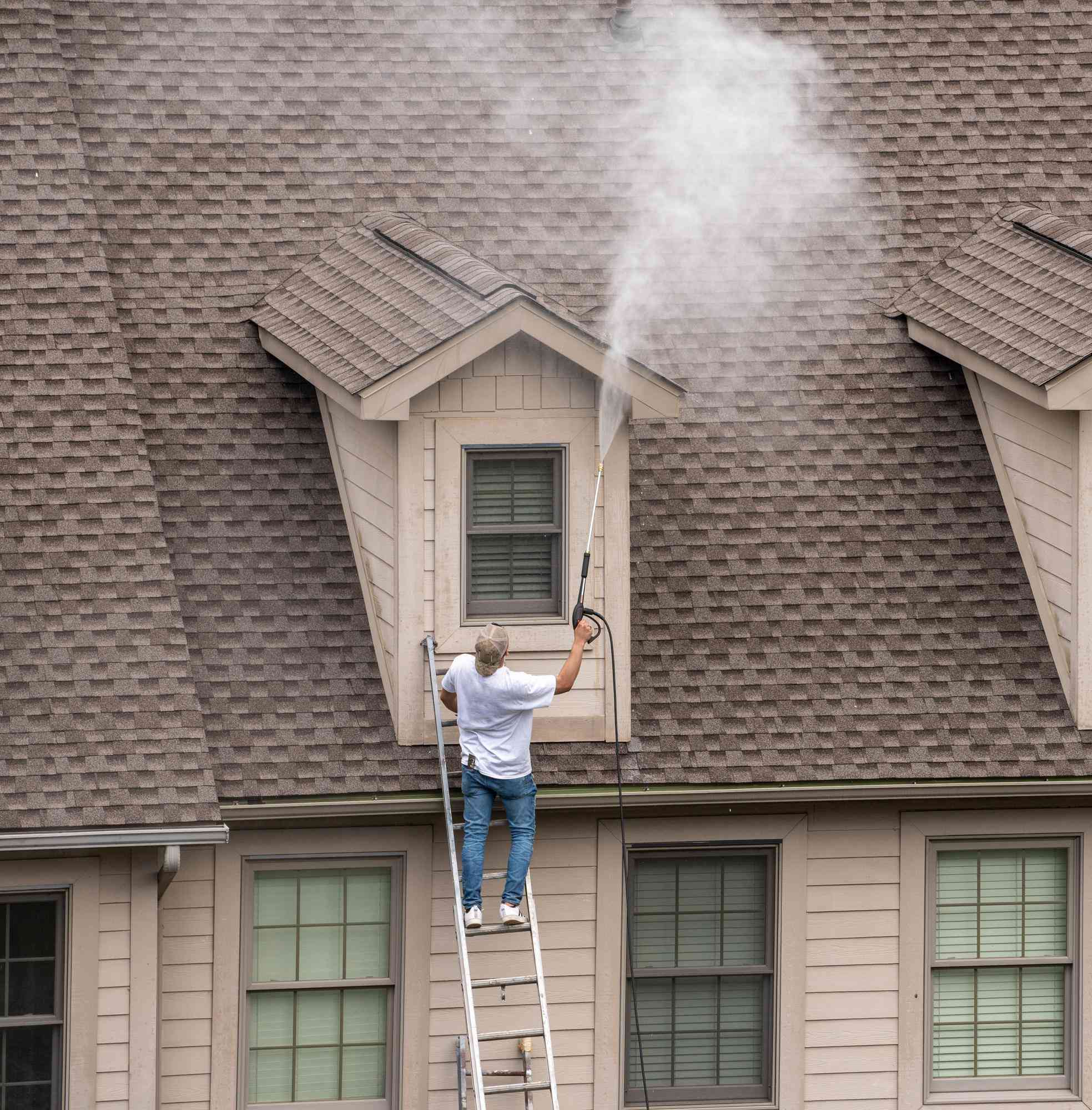 Worker on a ladder pressure washing the roof and dormer of a house